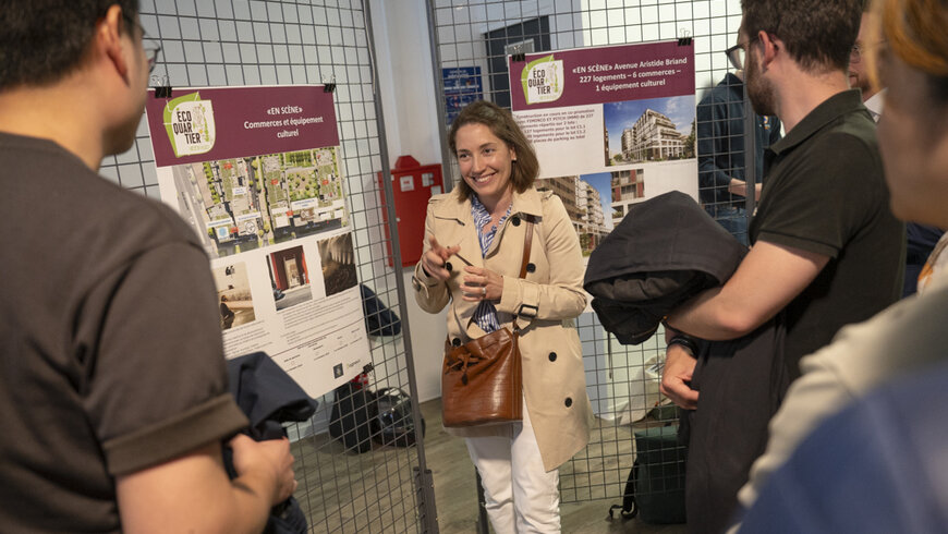 Devant des panneaux explicatifs des travaux, une dame expose le projet à trois personnes
