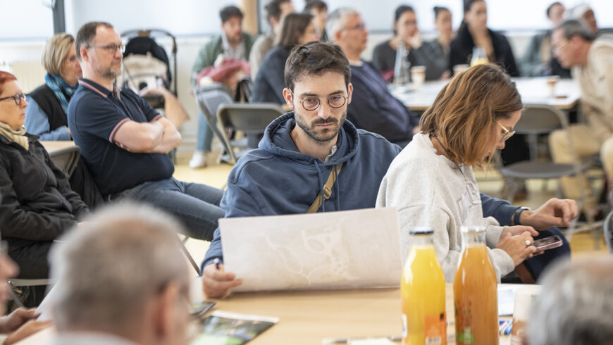 Gros plan sur une des tables, un homme lit le plan du parc Robespierre.