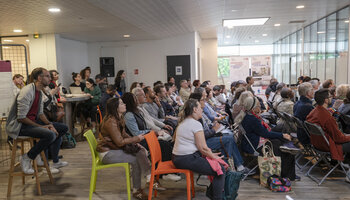 la foule rassemblée dans la salle regarde une présentation diffusée sur un écran devant eux