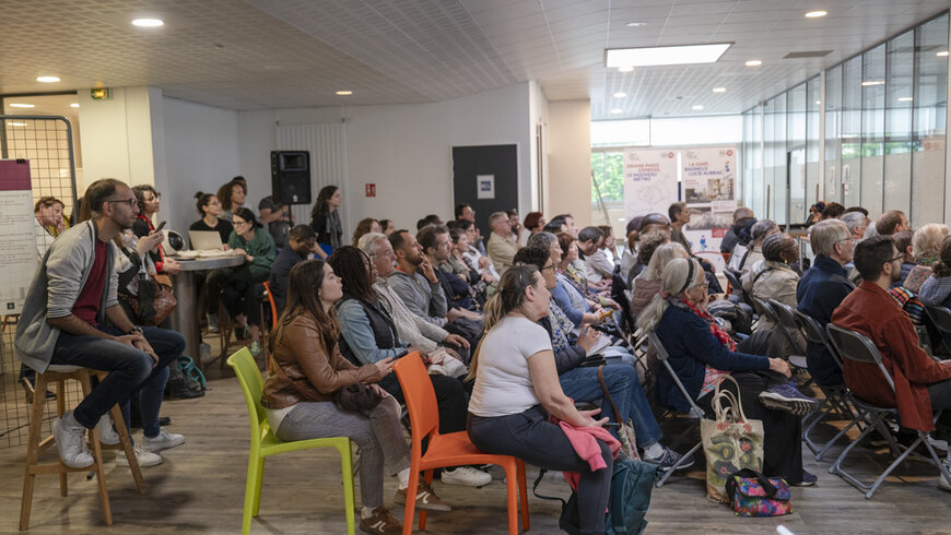 la foule rassemblée dans la salle regarde une présentation diffusée sur un écran devant eux