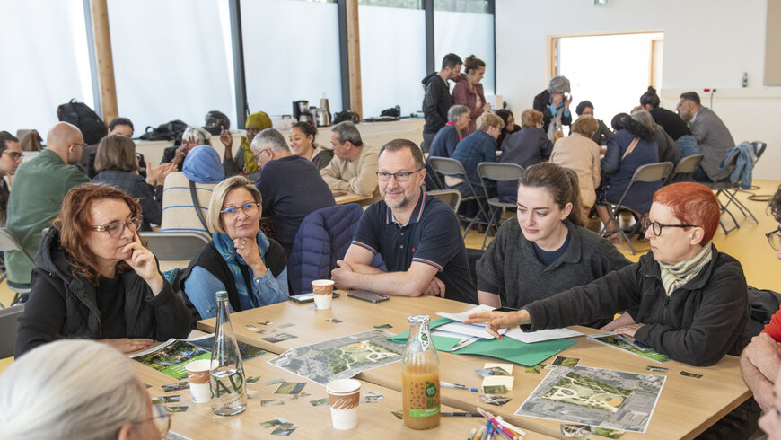 Gros plan sur une des tables. les gens regardent le plan du parc ainsi que des vignettes représentant des végétaux et différents élément de mobilier urbain. 