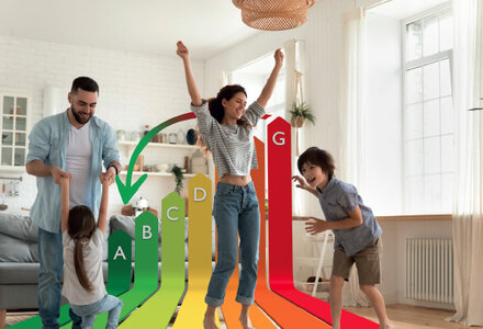 une famille, deux parents jouent avec leur deux jeunes enfants. Ils sont heureux. en fond d'image on le baromètre de la qualité énergétique noté de A à G